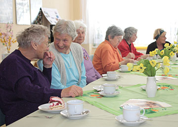 Foto: Seniorinnen sitzen am Tisch, essen Kuchen, lachen und unterhalten sich.