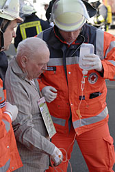 Foto: Zwie DRK-Helfer stützen einen älteren Mann und halten seine Tropf.